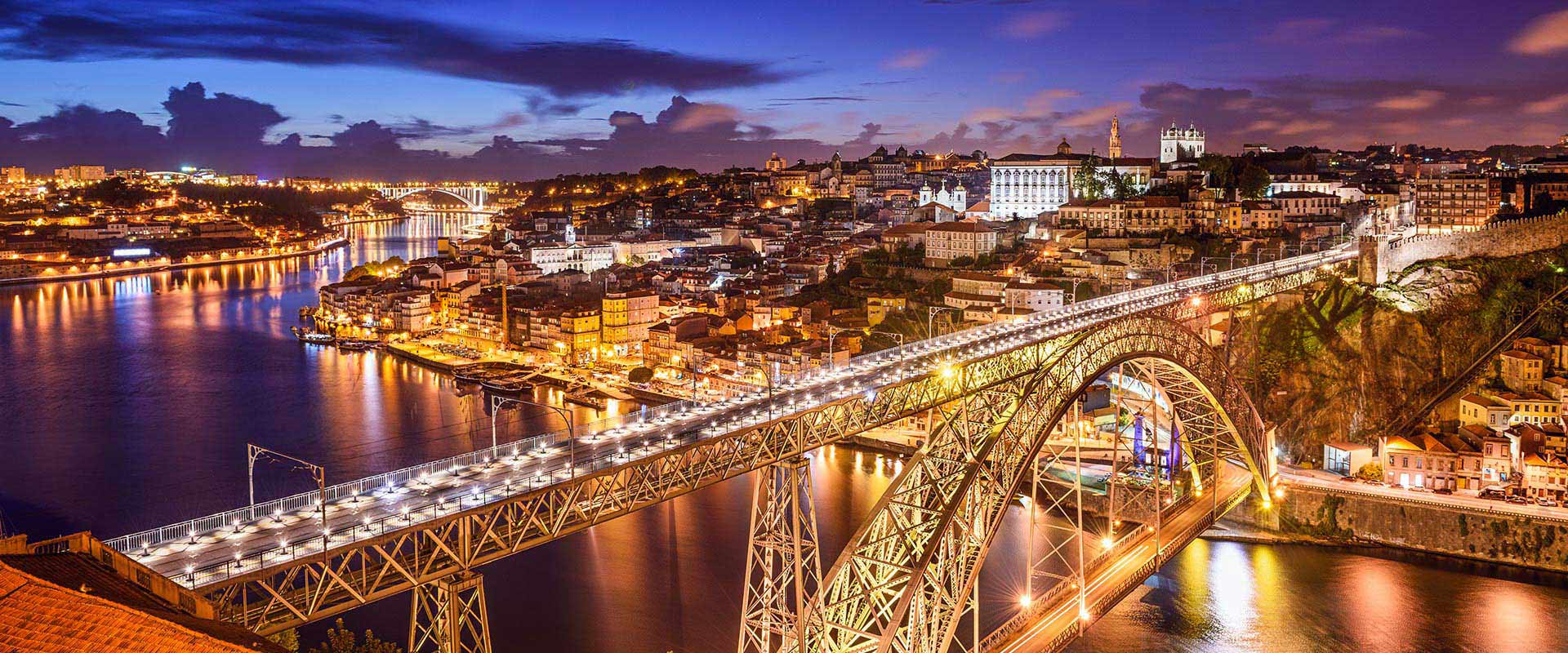 Vue nocturne du pont Dom Luís I sur le Douro à Porto, Portugal, avec la ville illuminée et des reflets dans l'eau.